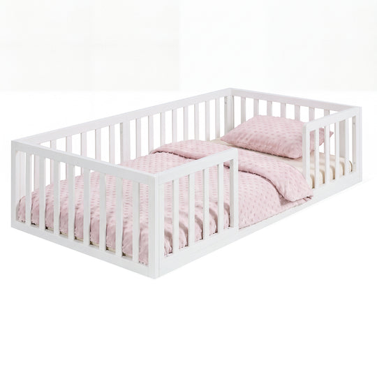 Weiß lackiertes Bodenbett aus Holz mit Rausfallschutz und rosa Punkte-Bettwäsche, freigestellt. Vollständig KI-generiert.