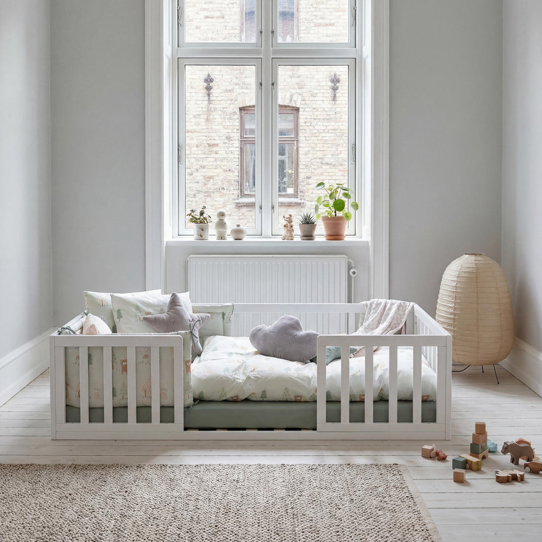 Weiß lackiertes Montessori-Bodenbett am hohen Fenster mit Papierlampe, Stern- und Wolkenkissen. Teilweise KI-generiert.