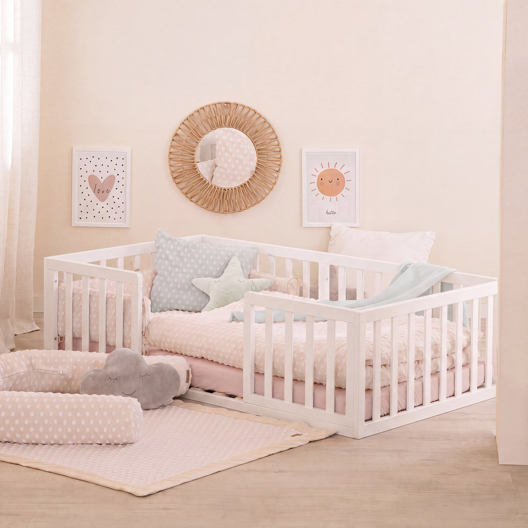 Weiß lackiertes Montessori-Bodenbett im beigen Kinderzimmer mit Rattanspiegel, Sternkissen und rosa Bettwäsche