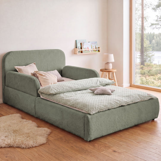 Lit enfant roba Little Dream vert sauge dans une chambre d'enfant avec vue sur le lac, bibliothèque et tapis en peau de mouton. Partiellement générée par IA.